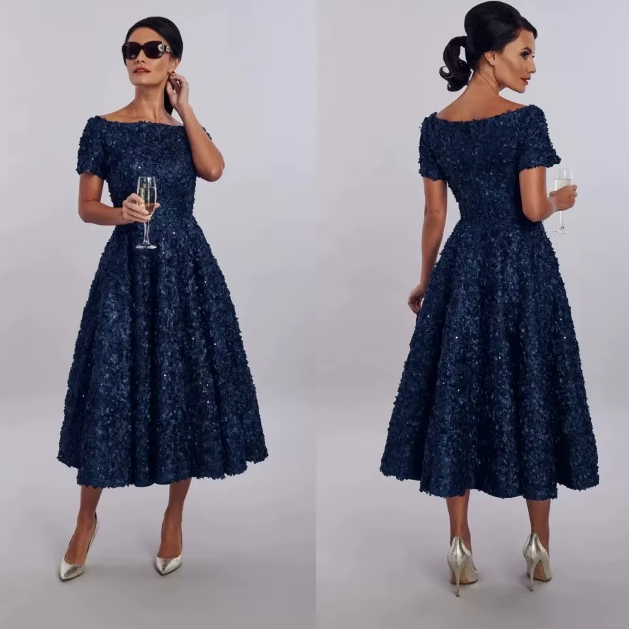 Woman wearing a navy blue dress with short sleeves and a full skirt, holding a glass of champagne on a white background.